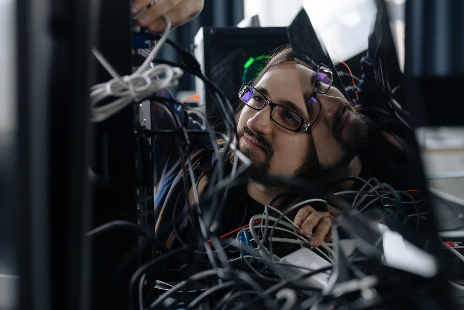 IT-Techniker prüft die Verkabelung hinter mehreren Computermonitoren